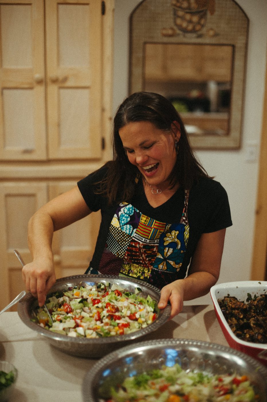 Gwen laughing while mixing a big bowl of salad