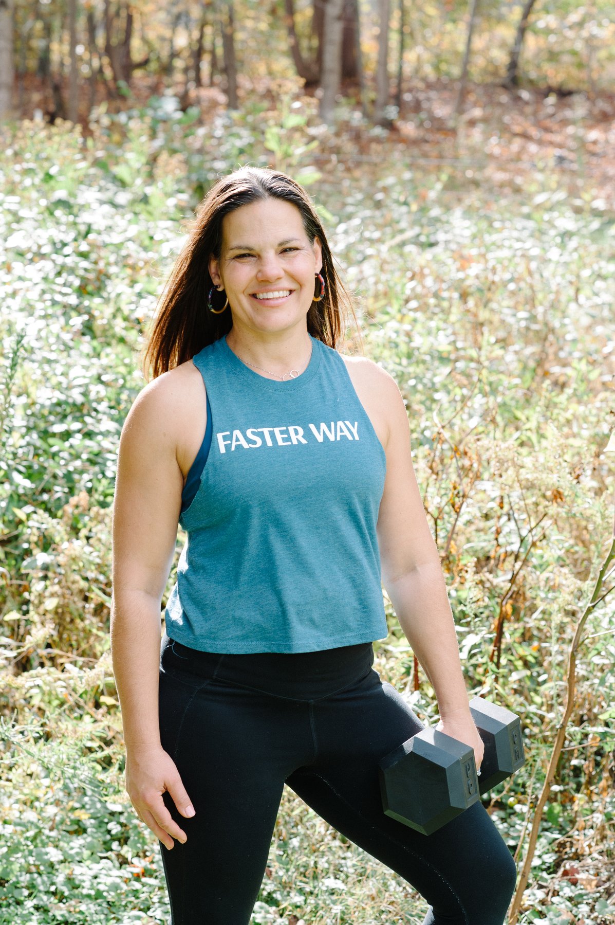 Gwen in a FASTer Way tank top holding a dumbbell outdoors